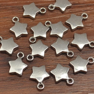 May include: A collection of 14 silver star-shaped charms with jump rings. The charms are scattered on a wooden surface.