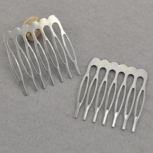 Op de afbeelding: Twee zilveren metalen haar kammen met elk zeven tanden. De kammen zijn ontworpen met een decoratieve, gebogen vorm.