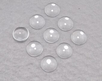May include: Eight clear glass cabochons, each with a slightly domed shape, arranged in a scattered pattern on a gray surface.