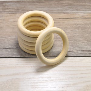 May include: A stack of 10 natural wood rings, each ring is about 2 inches in diameter. The rings are stacked on a light brown wooden surface.