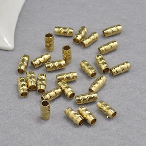 Pode incluir: Um grupo de 20 tampas de extremidade de cordão ou joias de metal dourado. As tampas têm um padrão texturizado em forma de diamante.