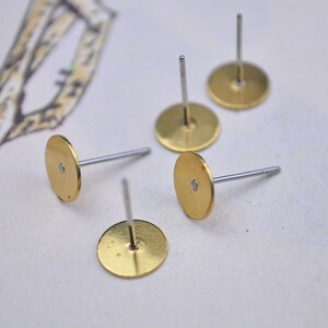 Puede incluir: Cuatro bases de pendientes de oro con postes de plata. Las bases de pendientes son redondas y tienen una superficie lisa.