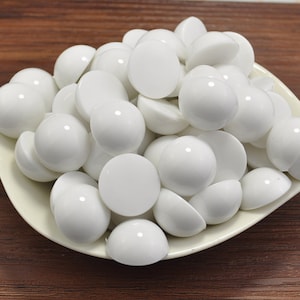 May include: A white bowl filled with white round plastic cabochons. The cabochons are smooth and shiny.