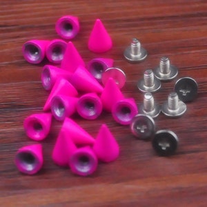 May include: A collection of pink cone-shaped studs with silver screws. The studs have a shiny, metallic finish and are arranged on a wooden surface.