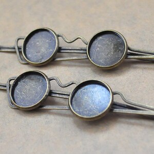 May include: Two antique gold-toned metal hair clips with round glass cabochon settings. The clips are designed to hold a round piece of glass or a cameo.