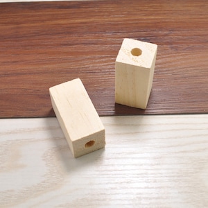 Puede incluir: Dos bloques de madera sin terminar con un agujero perforado en el centro. Los bloques son de color marrón claro y tienen una superficie lisa.
