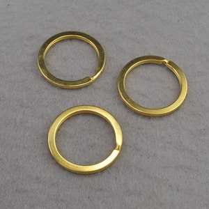 Op de afbeelding: Drie gouden metalen sleutelringen. De sleutelringen zijn allemaal even groot en even gevormd en zijn in een rij gerangschikt.