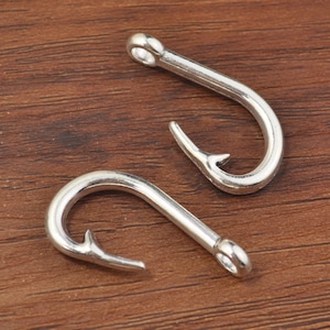 Op de afbeelding: Twee zilveren metalen vishaken op een houten oppervlak.