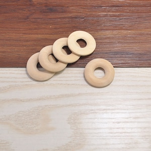 May include: Five wooden rings with a hole in the center, stacked on top of each other on a light brown wooden surface.