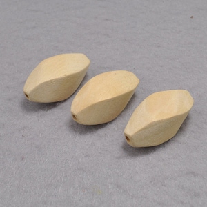 Könnte beinhalten: Drei Holzperlen in hellbeige. Die Perlen sind oval geformt und haben eine glatte, leicht strukturierte Oberfläche.
