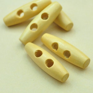 Puede incluir: Cinco botones de madera con dos agujeros cada uno. Los botones son de color marrón claro y tienen un acabado liso y pulido.