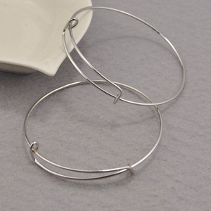 May include: Two silver bangle bracelets with a spring clasp closure. The bracelets are stacked on top of each other.