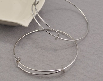 May include: Two silver bangle bracelets with a spring clasp closure. The bracelets are stacked on top of each other.