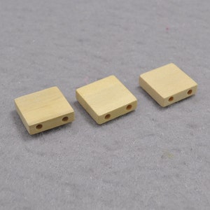 Puede incluir: Tres cuadrados de madera sin terminar con dos agujeros cada uno. Los cuadrados son de color marrón claro y tienen una superficie lisa.