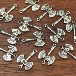 May include: A collection of silver-toned axe-shaped charms with double-sided loops. The charms are detailed with a textured surface and are perfect for jewelry making or crafting.