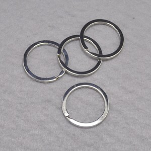 May include: Four silver key rings, each with a circular shape, are stacked on top of each other. The rings are made of metal and have a smooth, shiny finish.