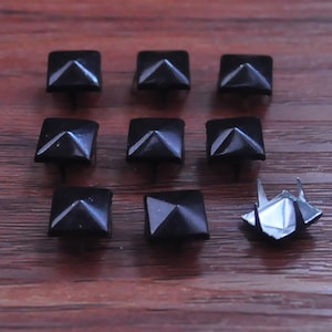 Può includere: Otto borchie nere a forma di piramide con base quadrata, e una borchia argentata a forma di piramide con base quadrata.