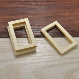 以下が含まれることがあります： 薄い茶色の木製の表面に、2つの木製の写真フレームが置かれています。1つは重ねて置かれ、もう1つは平らに置かれています。フレームは薄いベージュ色です。