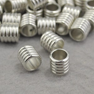 May include: A group of silver metal beads with a ridged design. The beads are about 1 inch in diameter and have a hole in the center.