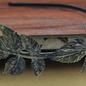 May include: A gold-toned metal headband with a leaf design. The leaves are detailed and have a textured finish.