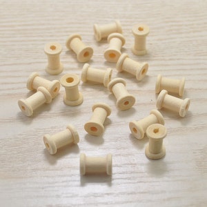 Può includere: Una collezione di bobine di legno di colore beige naturale. Le bobine sono sparse su una superficie di legno chiaro.