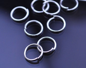 May include: A close-up of a group of silver jump rings. The rings are arranged in a random pattern on a dark blue surface.