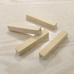 Puede incluir: Cuatro tacos de madera sin terminar con un agujero perforado en el centro de cada uno. Los tacos están dispuestos en un patrón aleatorio sobre una superficie de madera clara.