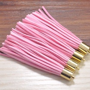 Puede incluir: Un conjunto de borlas de cuero rosa con puntas de metal dorado. Las borlas están dispuestas en una fila, con las puntas mirando hacia la cámara.