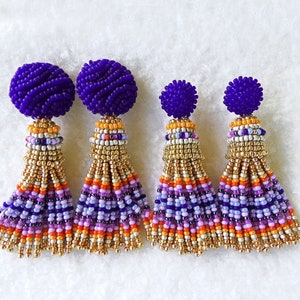 Puede incluir: Cuatro pares de pendientes de borla de cuentas moradas con detalles dorados. Las borlas est&aacute;n hechas de cuentas multicolores en tonos morados, rosas, naranjas y blancas.