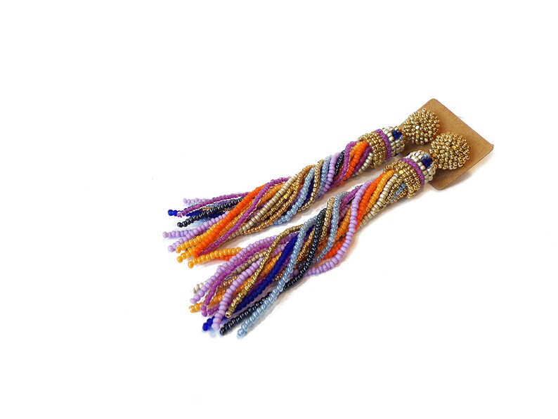 Puede incluir: Un par de pendientes largos de cuentas de colores con tapas doradas. Los pendientes est&aacute;n hechos con una variedad de colores, incluyendo morado, azul, naranja y dorado.