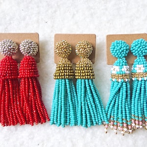 May include: Three pairs of tassel earrings. The first pair is red with silver tops. The second pair is turquoise with gold tops. The third pair is turquoise with white and gold accents.