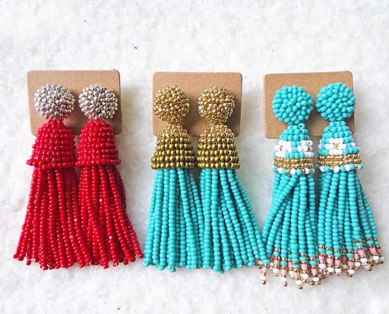 May include: Three pairs of tassel earrings. The first pair is red with silver tops. The second pair is turquoise with gold tops. The third pair is turquoise with white and gold accents.