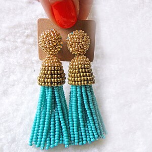 May include: A pair of turquoise and gold tassel earrings. The earrings are made of small beads and have a gold top.