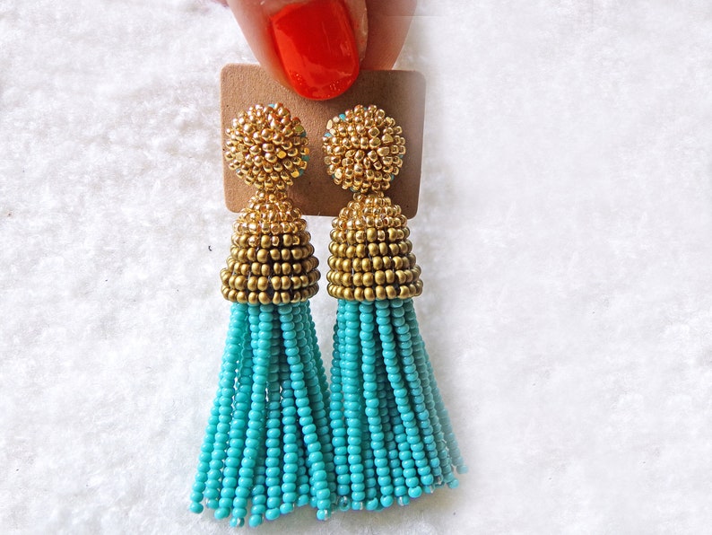 May include: A pair of turquoise and gold tassel earrings. The earrings are made of small beads and have a gold top.