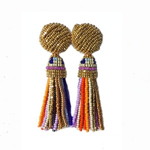 Puede incluir: Un par de pendientes de cuentas doradas con borlas de colores. Las borlas est&aacute;n hechas de peque&ntilde;as cuentas en tonos naranja, morado, azul y blanco.