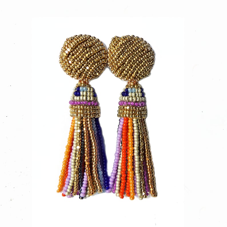 Puede incluir: Un par de pendientes de cuentas doradas con borlas de colores. Las borlas est&aacute;n hechas de peque&ntilde;as cuentas en tonos naranja, morado, azul y blanco.