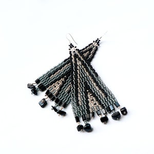 May include: A pair of long, beaded earrings with black, silver, and gray beads. The earrings have a tassel-like design and are finished with black gemstone accents.