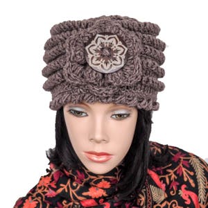 May include: A brown crocheted hat with a large, decorative, wooden button in the center. The button has a floral design with a white center.
