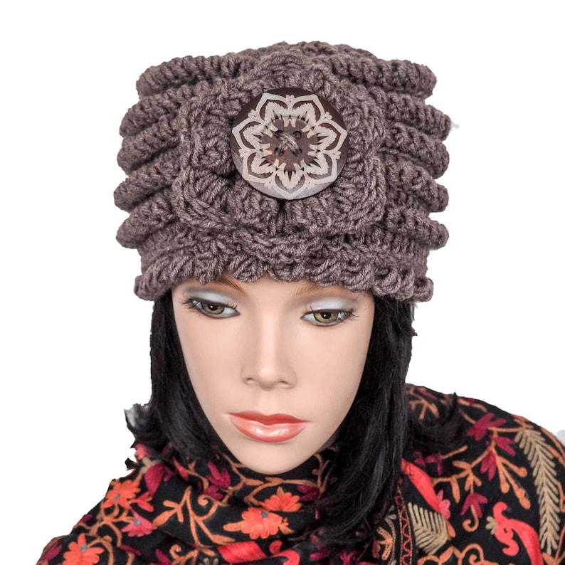 May include: A brown crocheted hat with a large, decorative, wooden button in the center. The button has a floral design with a white center.