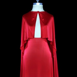 May include: A long, flowing red satin gown with a matching cape. The cape has a keyhole neckline and ties at the neck.