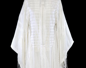 Puede incluir: Un vestido maxi blanco con una larga cremallera en la parte delantera y detalles de flecos en las mangas y el dobladillo.