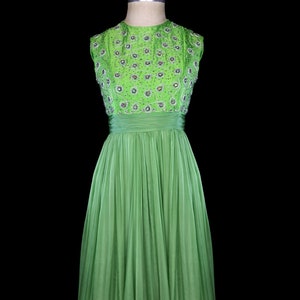 May include: A sleeveless green gown with a beaded bodice and a full skirt. The gown is on a mannequin against a black background.