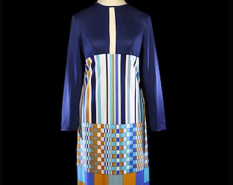 Pode incluir: Um vestido de manga comprida com um padrão geométrico em tons de azul, branco e laranja. O vestido tem um corpete justo e uma saia fluida.