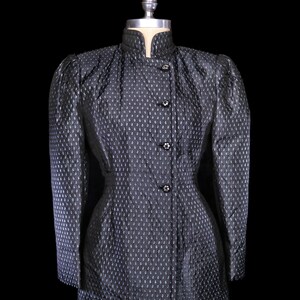 May include: A black quilted jacket with a stand-up collar and button closure. The jacket has a fitted silhouette and a subtle pattern of small white dots.