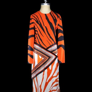 May include: A long-sleeved dress with a zebra print in orange and black. The dress has a wrap-style skirt with a geometric pattern in orange, black, and white.