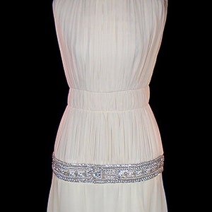 May include: A white sleeveless gown with a beaded belt. The gown is pleated and has a flowing skirt.