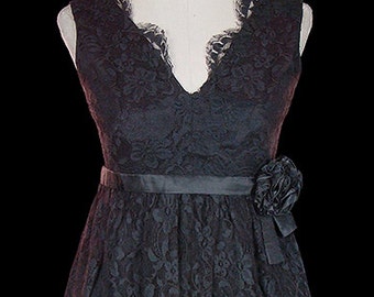 Puede incluir: Un vestido de encaje negro con escote en V y una cinta de satén negro. El vestido tiene un estampado floral y un dobladillo festoneado.