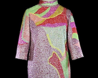 Pode incluir: Um vestido de lantejoulas rosa, verde, amarelo e vermelho com um padrão abstrato. O vestido tem um decote alto e mangas três quartos.