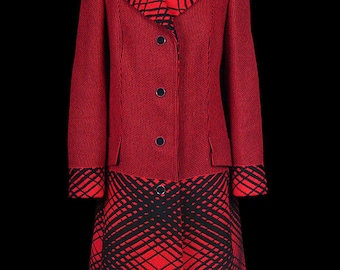 May include: A vintage red and black two-piece suit displayed on a mannequin. The suit features a red jacket with black geometric accents on the collar, cuffs, and skirt. The skirt has a matching geometric pattern. The suit is buttoned up.