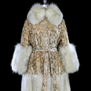 Puede incluir: Un abrigo de brocado dorado con cuello, puños y dobladillo de piel blanca. El abrigo tiene un cinturón y un estampado floral.